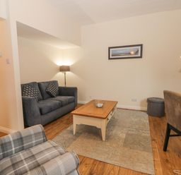 A living room with a grey sofa, plaid armchair, wooden coffee table, floor lamps, and dining chairs at Bugle in Saltburn-By-The-Sea