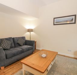 A sitting room with a gray sofa and patterned cushions a wooden coffee table a floor lamp a framed picture on the wall and a gray ottoman at Bugle in Saltburn-By-The-Sea