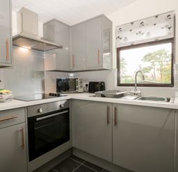 A kitchen with grey cabinets a stove microwave sink and a window with a sheep patterned blind at Lavender Lodge in Saltburn-By-The-Sea