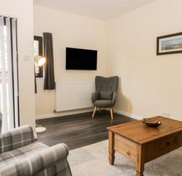 A living room with a plaid armchair a wooden coffee table a wall-mounted TV a gray armchair and a floor lamp at Lavender Lodge in Saltburn-By-The-Sea