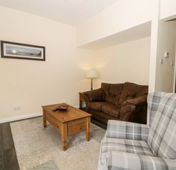 A living room with a brown sofa a plaid armchair a wooden coffee table and a framed picture on the wall at Lavender Lodge in Saltburn-By-The-Sea