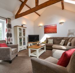A living room with a brown sectional sofa two armchairs a wooden coffee table a TV on a stand and a cabinet with glass doors at Littleham Court Cottage in Littleham near Bideford