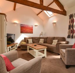 A living room with brown sofas a wooden coffee table a television and curtains at Littleham Court Cottage in Littleham near Bideford