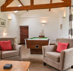 A sitting area with two armchairs red cushions and a pool table at Littleham Court Cottage in Littleham near Bideford