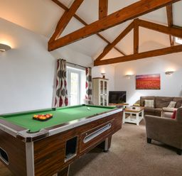 A living room with a pool table sofa a television and wooden beams at Littleham Court Cottage in Littleham near Bideford
