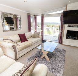 A living room with two sofas a glass coffee table a mounted television and fireplace and a door leading to a balcony at Crosswinds 67 in Bembridge
