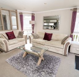 A living room with two beige sofas pillows a glass coffee table and purple curtains at Crosswinds 67 in Bembridge