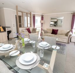 A dining table set for four with plates and cutlery in a living room with sofas and purple curtains at Crosswinds 67 in Bembridge
