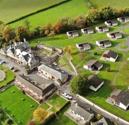 An aerial view of a property with multiple small buildings and a large central building surrounded by green fields at Harcombe House Bungalow 3 in Chudleigh