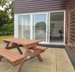 A wooden picnic table on a patio outside sliding glass doors of a brown building at Harcombe House  Bungalow 4 in Chudleigh
