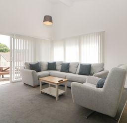 A living room with a gray sectional sofa, armchair, wooden coffee table, vertical blinds, and sliding glass door at Harcombe House Bungalow 4 in Chudleigh