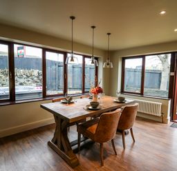 A dining area with a wooden table and four chairs by large windows and a glass door at Dant Y Llew in Bow Street Wales