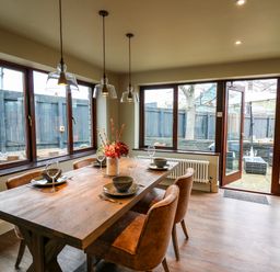 A dining room with a wooden table set with plates bowls and wine glasses next to large windows and glass doors at Dant Y Llew in Bow Street Wales