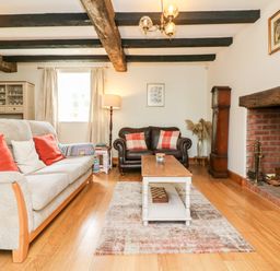 A living room with a sofa and armchair near a fireplace and wooden beams on the ceiling at Home Farm Cottage in Fremington Devon