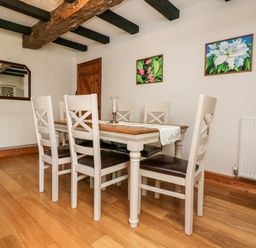 A dining room with a wooden table and six chairs under exposed ceiling beams at Home Farm Cottage in Fremington Devon