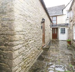 A stone paved courtyard between stone buildings with wooden and white doors at Bobbin Cottage in Swanage