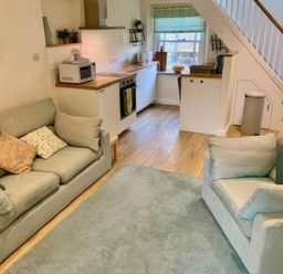 A living room with sofa and kitchen area at Bobbin Cottage in Swanage