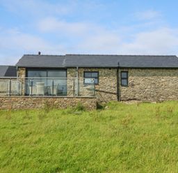 A stone house with a glass railing and outdoor furniture on a grass lawn at Tyddyn Bach in Rhydwyn