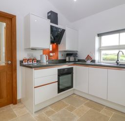 A kitchen with white cabinets black countertop an oven a kettle a knife block and a window at Tyddyn Bach in Rhydwyn