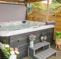 An outdoor hot tub with water jets under a wooden canopy with towels flowers a bottle of wine and glasses at Braeside Farm House in Cloughmills