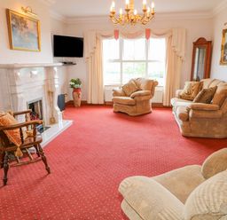 A living room with armchairs a sofa a wooden rocking chair a fireplace and a wall-mounted television at Braeside Farm House in Cloughmills