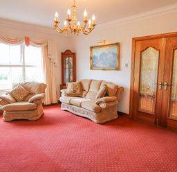 A living room with beige sofas a red carpet wooden double doors a chandelier and a glass display cabinet at Braeside Farm House in Cloughmills