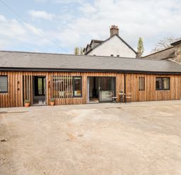 A wooden barn style house with stone walls and a concrete courtyard at 1 Caddaford Barns in Buckfastleigh