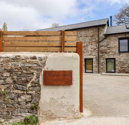 Exterior of a stone building with a sign reading caddaford barns and a wooden fence at 1 Caddaford Barns in Buckfastleigh