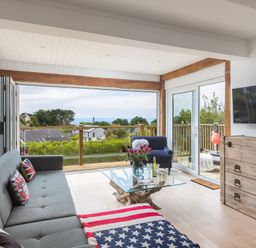 A living room with a gray sofa and American flag blanket by a glass table with flowers and a wooden chest at Trewartha in Praa Sands