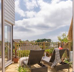 A balcony with two lounge chairs and potted plants overlooking rooftops at Trewartha in Praa Sands