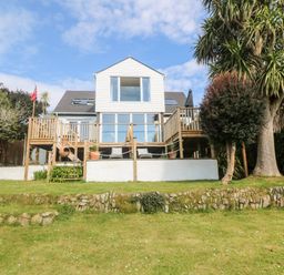 A two-story house with a wooden deck overlooking a grassy lawn with trees and stone edging at Trewartha in Praa Sands