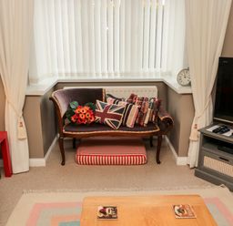 A living room corner with a small vintage sofa with cushions and a striped pet bed underneath at Tartaria in Widdrington