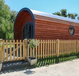 An outdoor wooden pod with a curved roof behind a wooden picket fence with two potted plants at Willow Pod in Arundel West Sussex