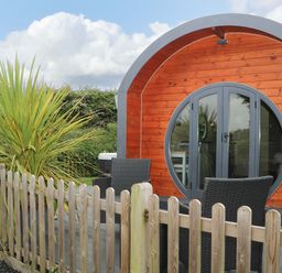 A wooden pod with round doors and outdoor seating behind a wooden fence at Willow Pod in Arundel West Sussex