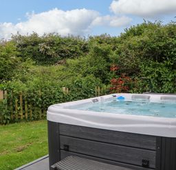 An outdoor hot tub on a deck next to a green garden with a wooden fence at Willow Pod in Arundel West Sussex