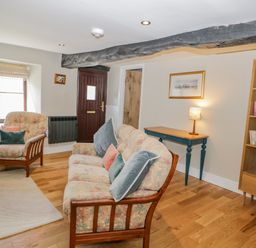 A sitting room with a floral sofa and armchair next to a window a wooden bookshelf and a small table with a lamp at Ashness in Bassenthwaite near Keswick