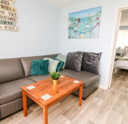 A living room with a gray sofa and wooden coffee table next to a bedroom at Cwtsh Cragen in New Quay