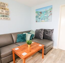 A corner of a living room with a gray sectional sofa with cushions and a wooden coffee table with a small plant at Cwtsh Cragen in New Quay
