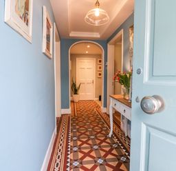 A hallway with blue walls a patterned tile floor a white door at the end and a table with flowers at 1 Tower House in Cartmel