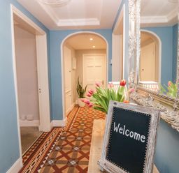 A hallway with blue walls patterned floor a bouquet of tulips and a welcome sign at 1 Tower House in Cartmel
