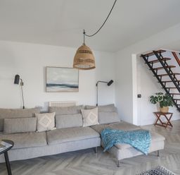 A living room with a gray sectional sofa and a blue throw next to wooden stairs at Disgwylfa in Moelfre