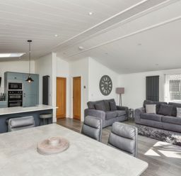 An open-plan living area with a kitchen, dining table, two sofas, wall clock, and a floor lamp at Gerrida Lodge in South Lakeland Leisure Village near Tewitfield