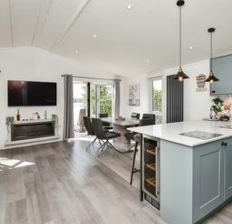 An open plan kitchen and dining area with blue cabinets a dining table with black chairs and a wall mounted television at Gerrida Lodge in South Lakeland Leisure Village near Tewitfield