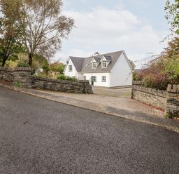 A white house with a grey roof behind stone walls and a paved driveway at Seascape Lodge in Kenmare County Kerry