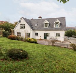 A two story house with a gray roof and white walls surrounded by grass and bushes at Seascape Lodge in Kenmare County Kerry