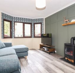 A living room with a blue sofa a television on a wooden stand and a black stove at Alfresco Lodge in Skiptory Howe 37B White Cross Bay near Windermere
