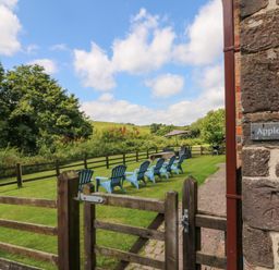 A fenced garden area with blue chairs arranged on the grass and a table with an umbrella at Apple Barn in South Molton