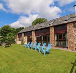 A stone and brick building with large windows and a row of blue chairs on the lawn with a picnic table and outdoor dining set at Apple Barn in South Molton