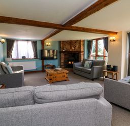 A living room with gray sofas a wooden coffee table a wall-mounted television and a brick fireplace at Apple Barn in South Molton