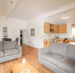 An open plan living room and kitchen with two grey sofas a wooden floor and dining table at Beside the Sea in Eype
